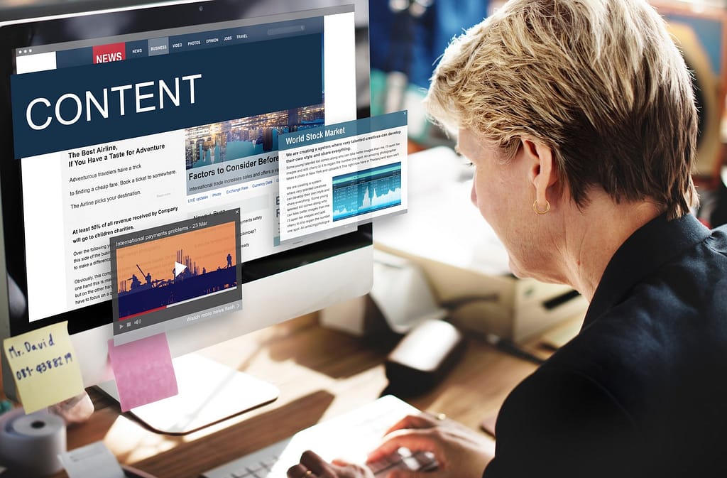 Woman working on a desktop computer displaying a 'CONTENT' website and various pop-up windows including articles and a video.
