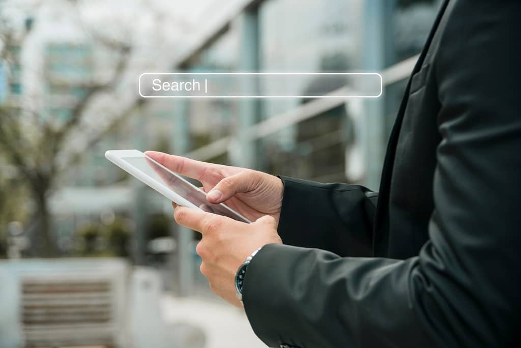 Person using a tablet device outdoors, with a digital search bar interface.