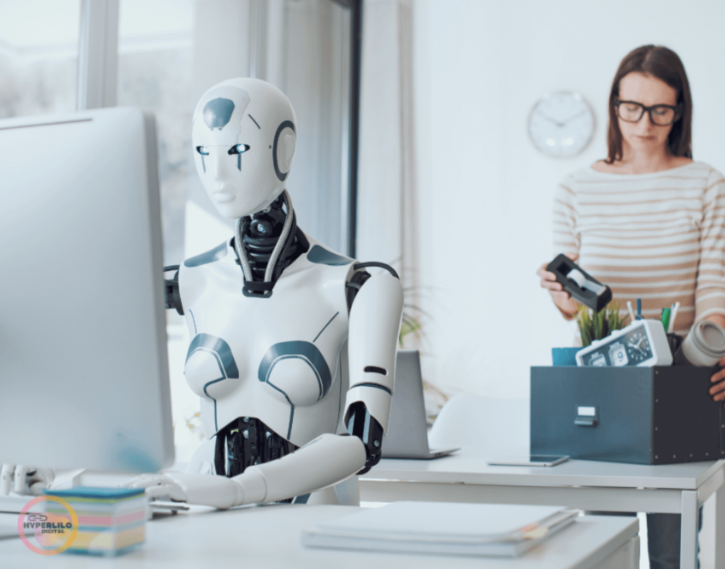 A humanoid robot works at a computer while a woman packs her belongings in the background.